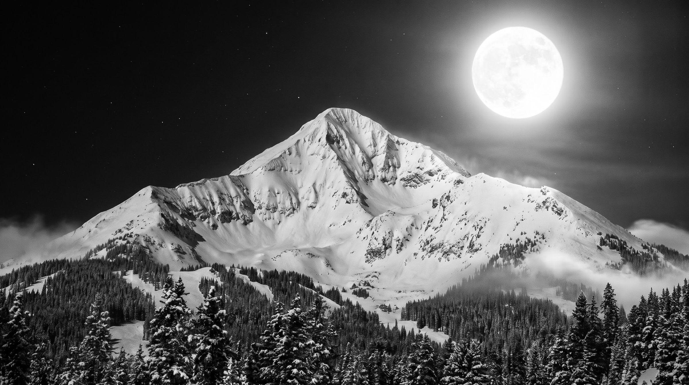 Snow-covered mountain under a full moon, black and white